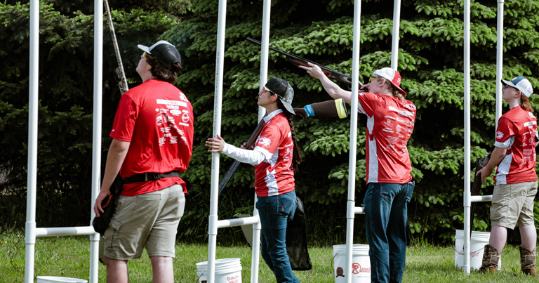 A group of people in red shirts standing in a field shooting.